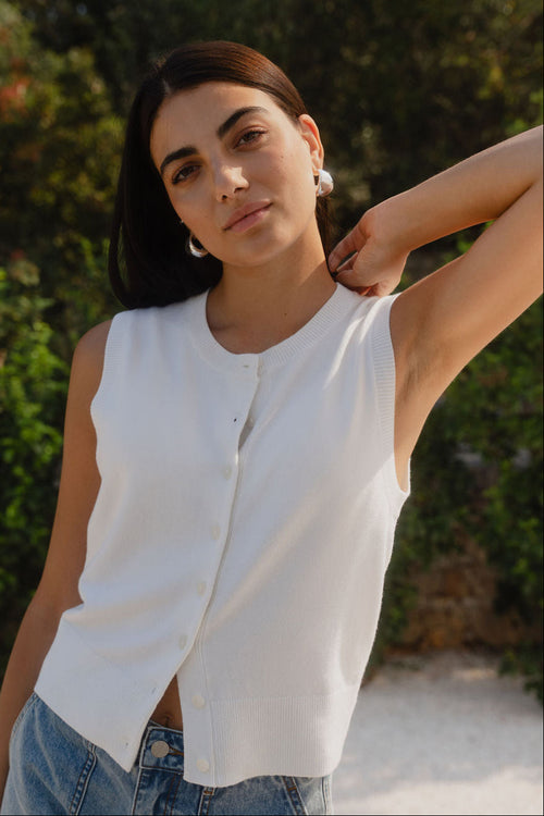 Woman wearing a white sleeveless top and blue jeans with a blurred green background