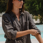 Woman standing by a poolside wearing sunglasses and a striped shirt.