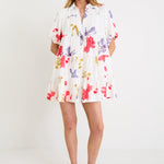 Model wearing a cream mini tiered shirt dress with colourful poppy floral print, puff sleeves and a button front.