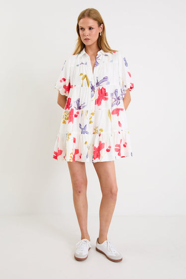 Model wearing a cream mini tiered shirt dress with colourful poppy floral print, puff sleeves and a button front.