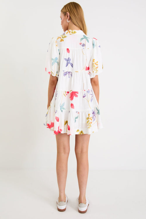 Model wearing a cream mini tiered shirt dress with colourful poppy floral print, puff sleeves and a button front.