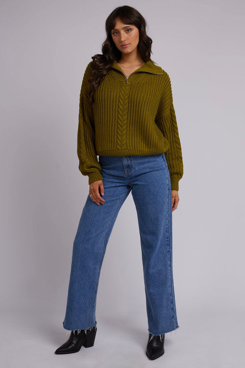 Model wears green knit and blue jeans