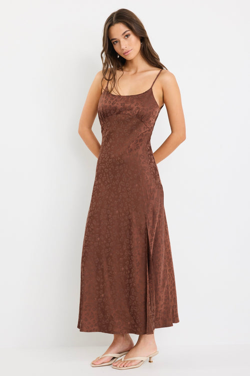 Woman wearing a chocolate brown strappy bias-cut midi dress with a subtle animal print and front slit, styled with cream heeled sandals.