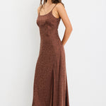 Woman wearing a chocolate brown strappy bias-cut midi dress with a subtle animal print and front slit, styled with cream heeled sandals.