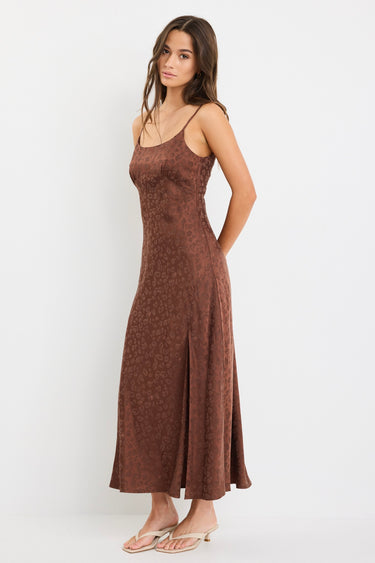 Woman wearing a chocolate brown strappy bias-cut midi dress with a subtle animal print and front slit, styled with cream heeled sandals.