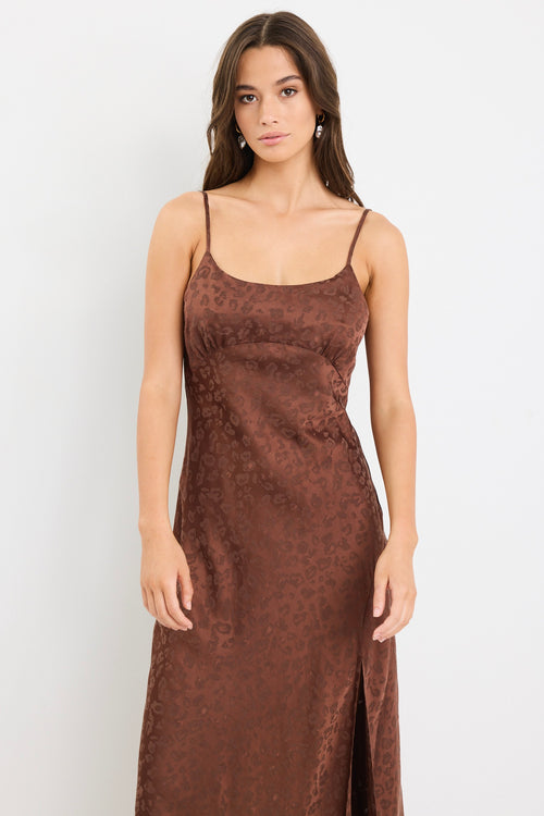 Woman wearing a chocolate brown strappy bias-cut midi dress with a subtle animal print and front slit, styled with cream heeled sandals.