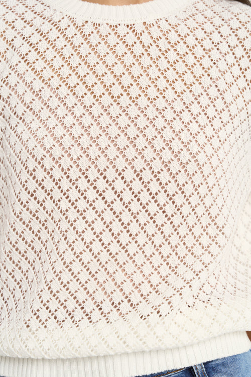 Woman wearing a short sleeve, open-knit ivory tee with a crew neck and light blue jeans.