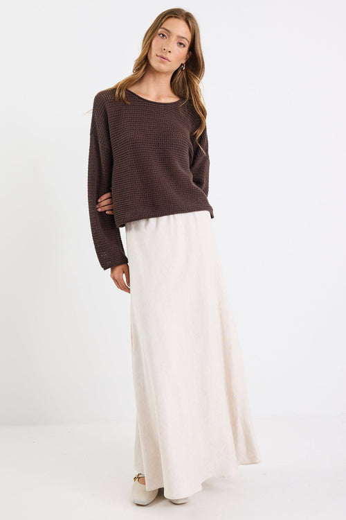 Woman wearing a brown sweater and white pants on a white background
