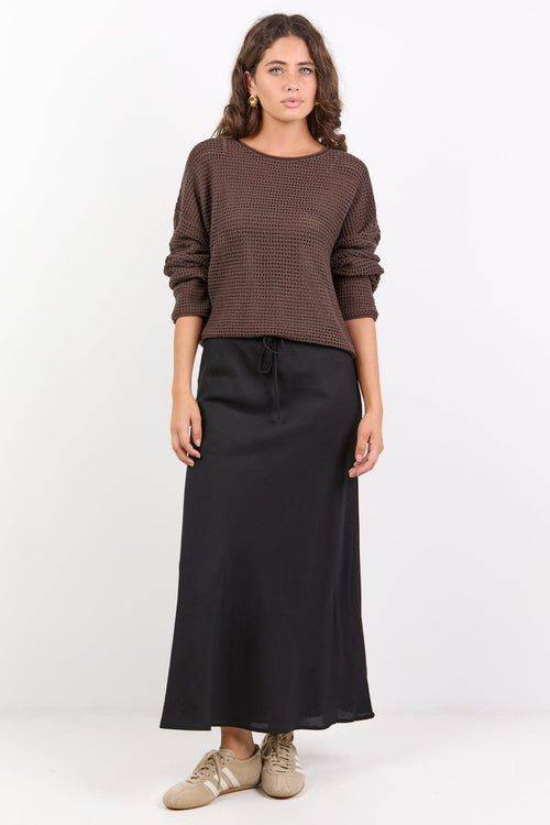 Woman wearing a brown sweater and black skirt on a white background