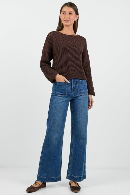 Woman wearing a brown textured sweater and blue jeans on a white background