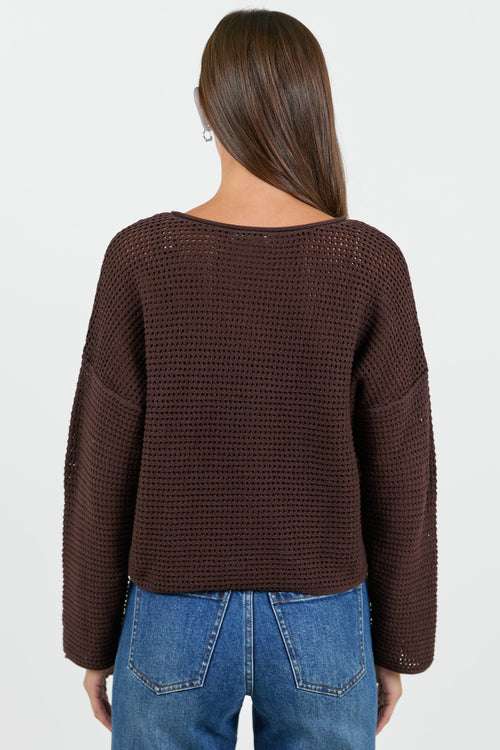 Person wearing a brown textured sweater and blue jeans on a white background