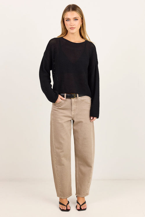 A woman modeling a black long-sleeve knit top and beige wide-leg pants against a plain white studio background.