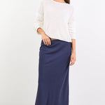 Woman wearing a white sweater and navy skirt on a white background