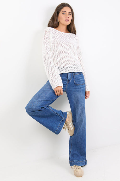 Woman wearing a white sweater and blue jeans against a white background
