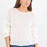 Woman wearing a white textured sweater and blue jeans on a light gray background