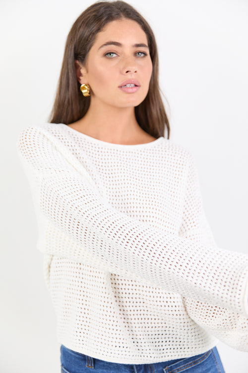 Woman wearing a white crochet sweater against a plain background