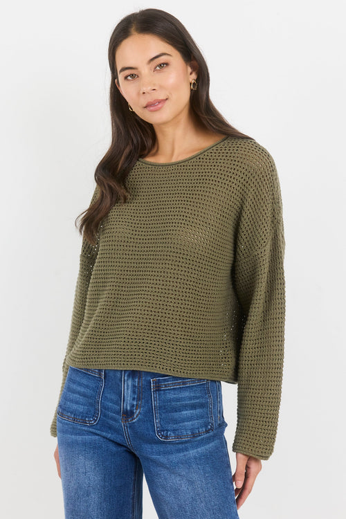 Woman wearing a green textured sweater and blue jeans on a white background