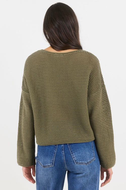 Person wearing a green textured sweater and blue jeans on a white background