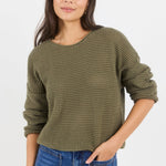 Woman wearing a green knitted sweater and blue jeans on a white background