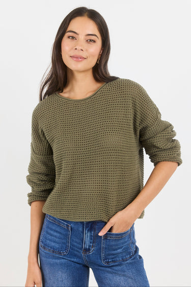 Woman wearing a green knitted sweater and blue jeans on a white background