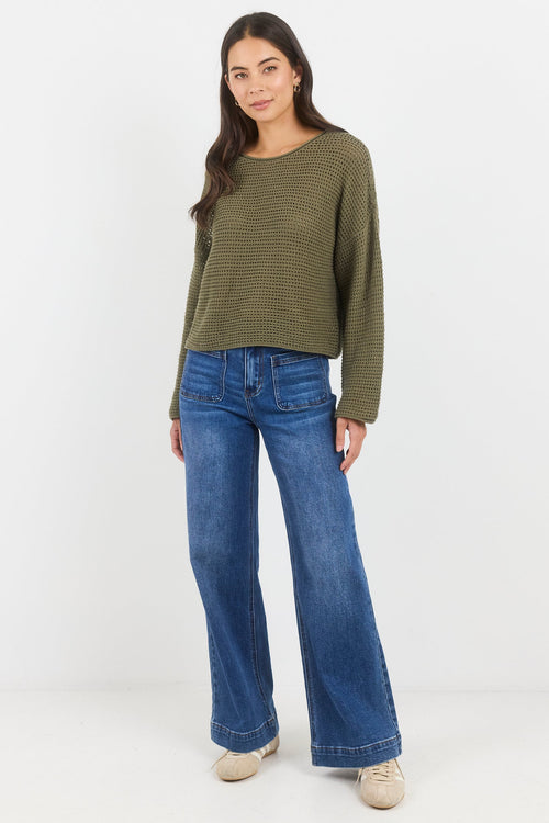 Woman wearing a green sweater and blue jeans on a white background