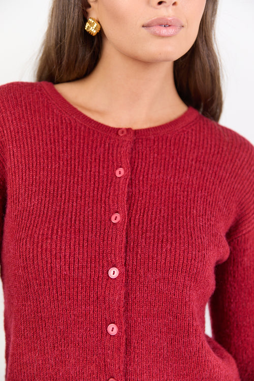 Close-up of a person wearing a red knitted cardigan with a plain background