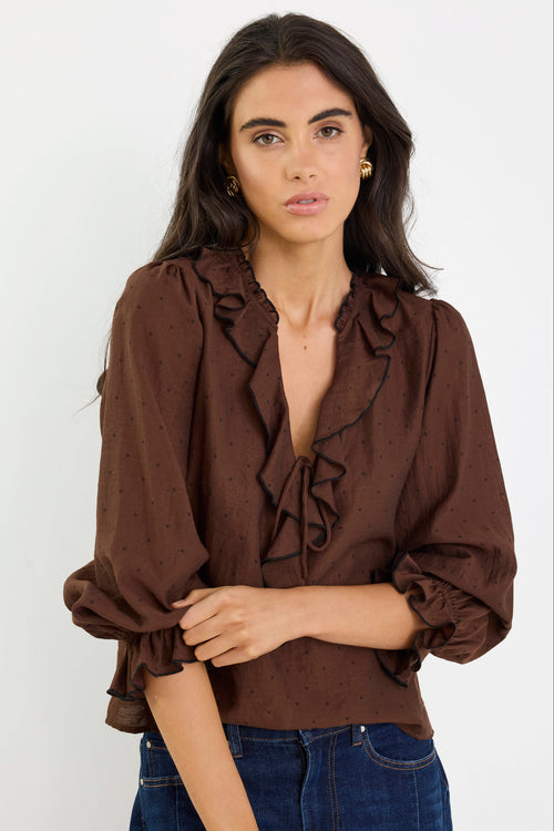 Woman wearing a brown blouse with ruffled details and blue jeans on a white background