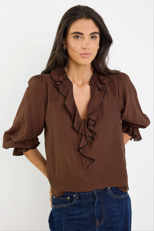 Woman wearing a brown blouse with ruffled details on a white background