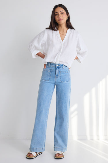 model wears light blue denim jeans and a white long sleeve top with white sandals