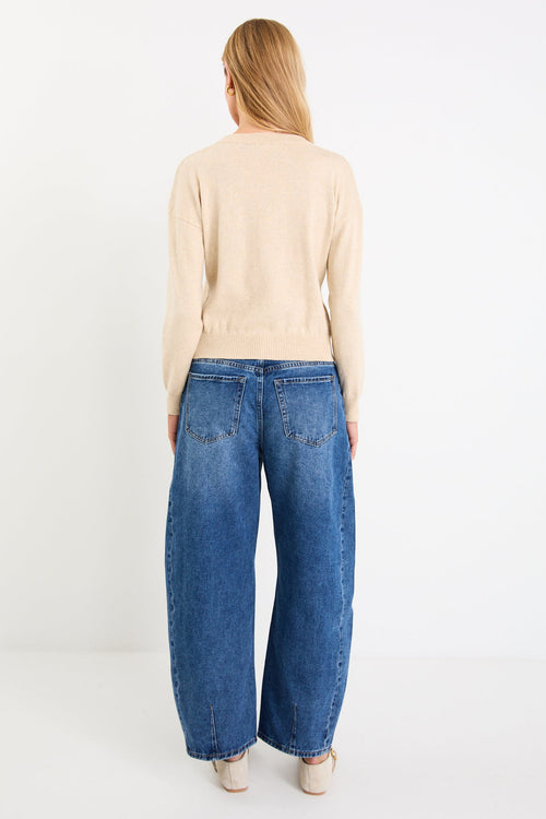 Woman wearing a beige sweater and blue jeans on a white background