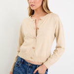 Woman wearing a beige cardigan and blue jeans against a white background