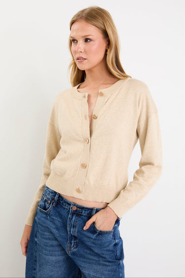 Woman wearing a beige cardigan and blue jeans against a white background