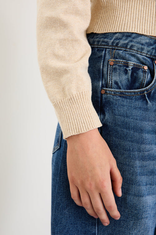 Person wearing a beige sweater and blue jeans on a plain background