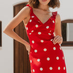 Woman wearing a red dress with white polka dots in an outdoor setting.