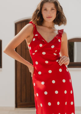 Woman wearing a red dress with white polka dots in an outdoor setting.