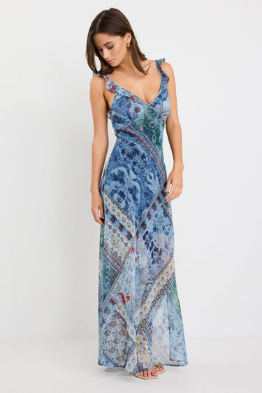 Woman wearing a blue maxi dress with a paisley scarf print, ruffle shoulder straps, and flowing bias-cut silhouette.