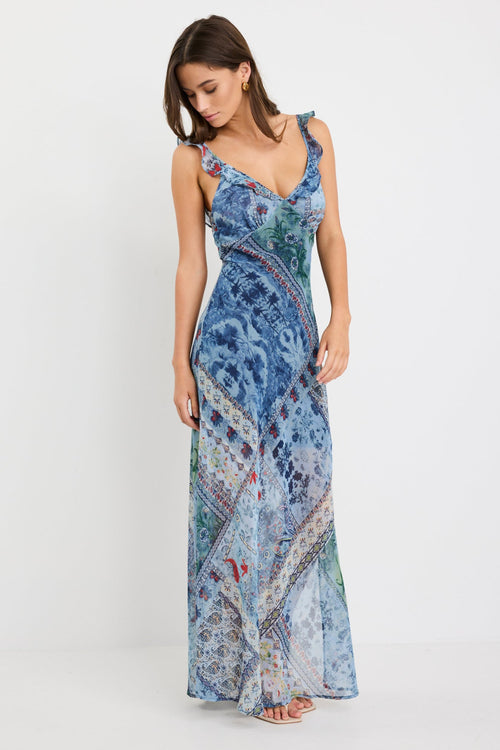 Woman wearing a blue maxi dress with a paisley scarf print, ruffle shoulder straps, and flowing bias-cut silhouette.
