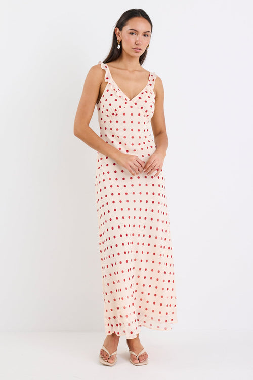 Woman wearing a cream and red polka dot slip maxi dress with adjustable straps, V-neckline, and a flowing bias-cut design.