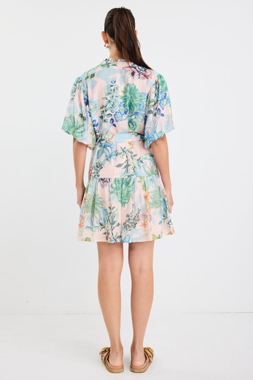 Woman wearing a colourful floral mini dress with a waist tie, short sleeves, and a tiered skirt.







