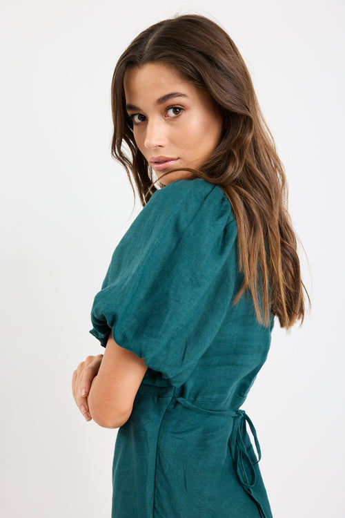 Woman wearing a forest green mini dress with puff sleeves, bias-cut shape, and fitted waist, styled simply for an elegant look.