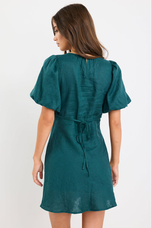 Woman wearing a forest green mini dress with puff sleeves, bias-cut shape, and fitted waist, styled simply for an elegant look.