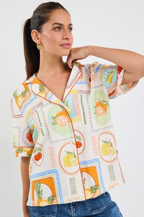 Woman wearing a colourful short sleeve blouse with postcard-style fruit prints and a button front, styled with blue jeans.
col_pattern