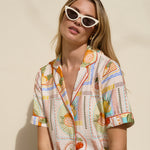 Woman wearing a colorful patterned shirt and sunglasses against a beige background