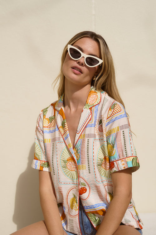 Woman wearing a colorful patterned shirt and sunglasses against a beige background