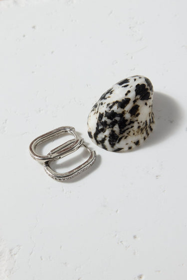 Two rings, one silver and one dalmatian jasper, on a textured white surface.