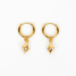 A pair of gold huggie hoop earrings with a small dangling geometric diamond-shaped charm, shown on a plain white background.