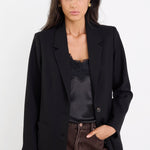 Woman wearing a black blazer over a black top with brown pants on a white background