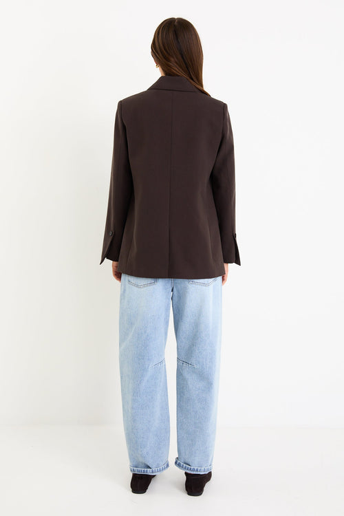 Model wearing a dark chocolate tailored blazer with a two-button front and vented sleeves.