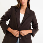 Woman wearing a brown blazer over a white shirt and blue jeans on a white background