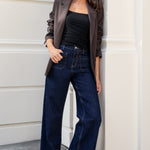 Woman in a black top and blue jeans leaning against a building wall.